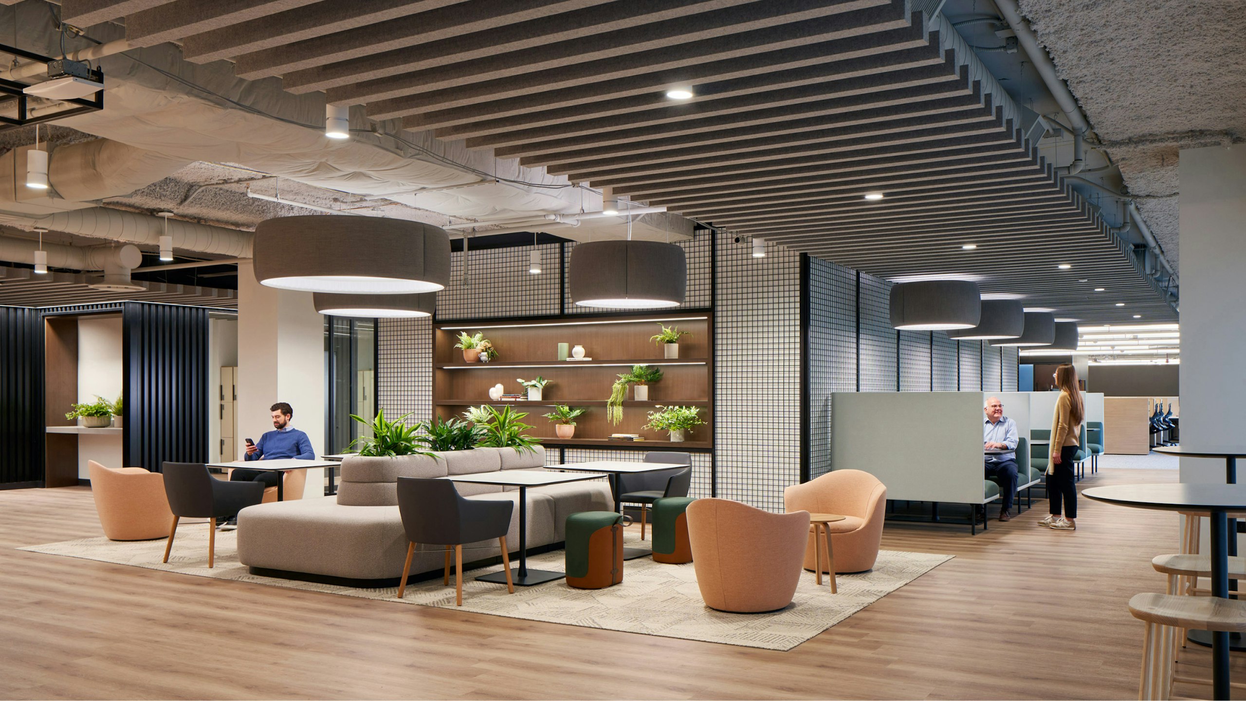 Several persons using a communal seating area with a variety of seating configurations including DWR Lina Swivel Chairs, private booths, and large grey bench seating