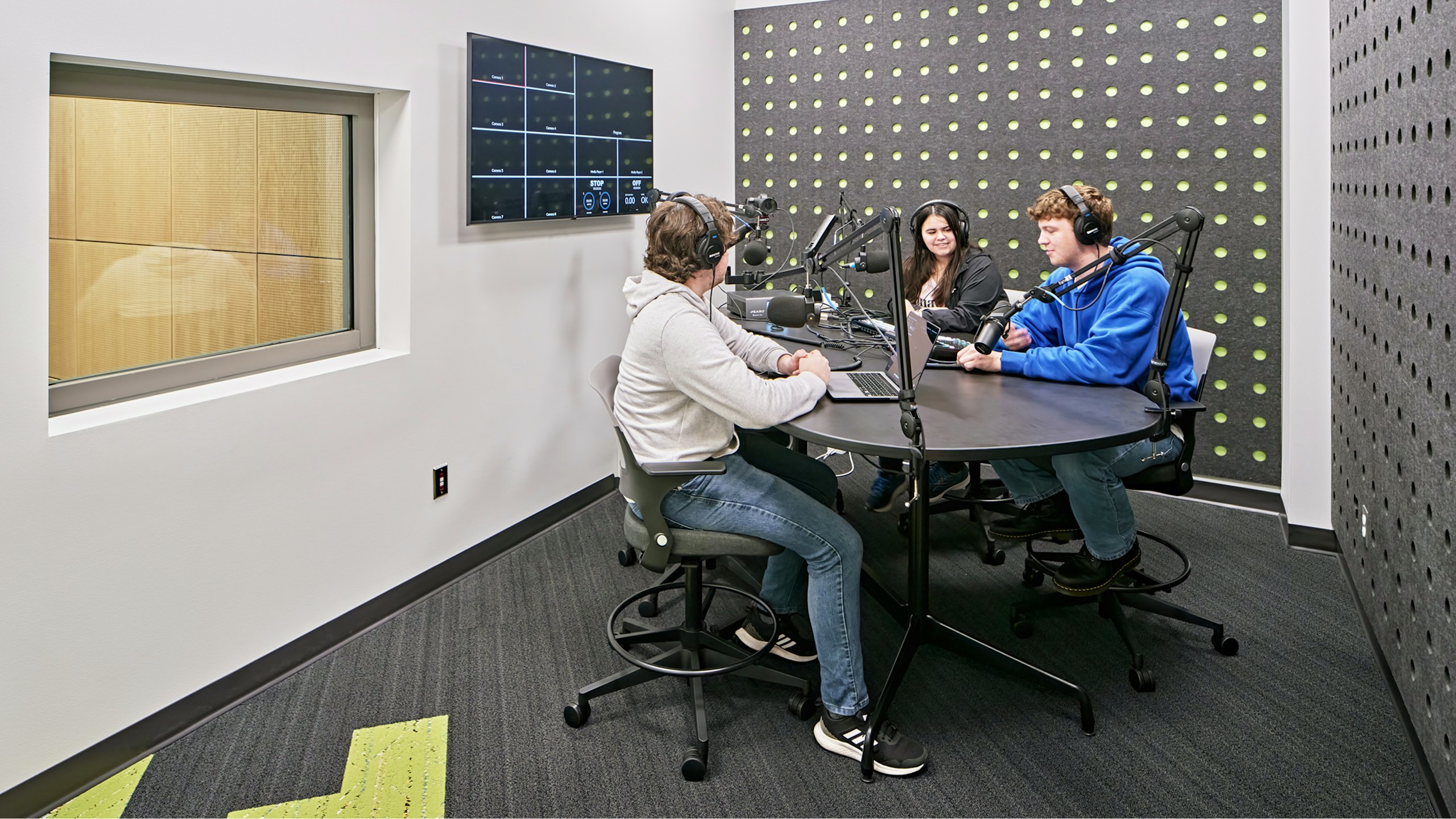 Three students sitting around a table and using recording equipment in an audio recording booth